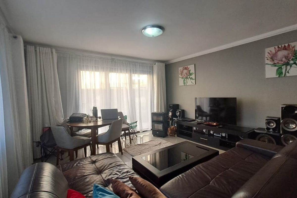 A comfortable living room featuring tiled flooring, large windows with sheer curtains, and neutral wall finishes, providing a functional and well-lit space.