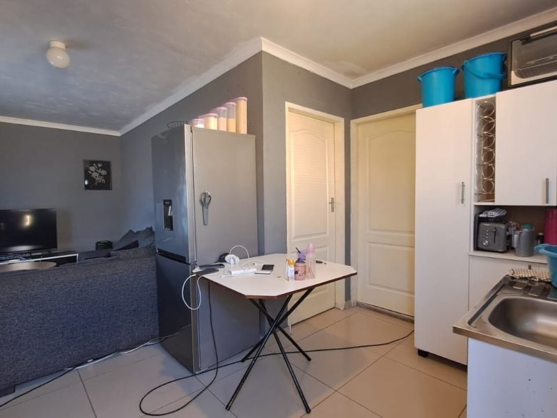 Open plan living area featuring tiled flooring, neutral grey walls, and a compact kitchen corner with built-in cabinetry and stainless steel sink.