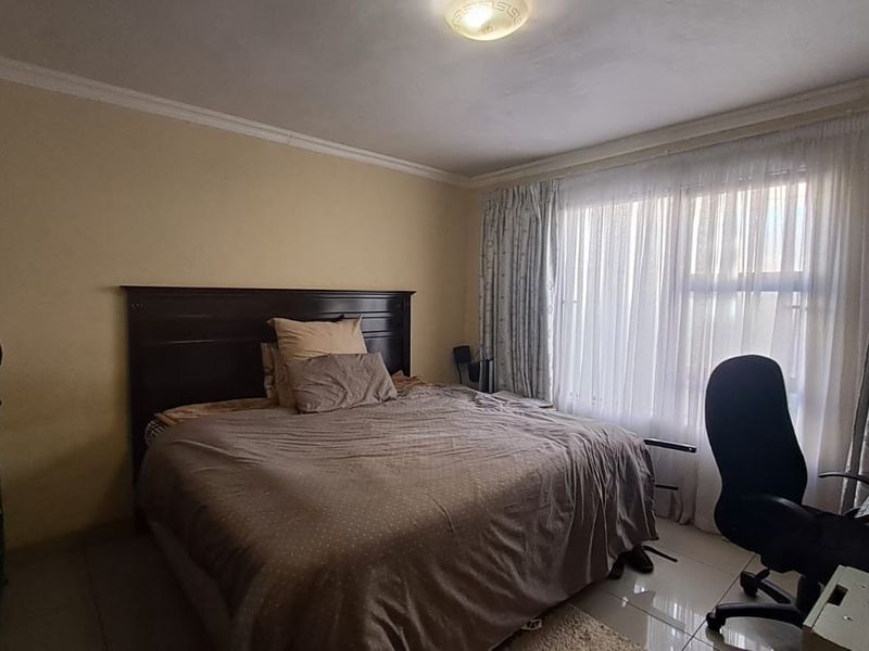 A functional bedroom featuring tiled flooring, a large window with curtain treatments, and crown molding.