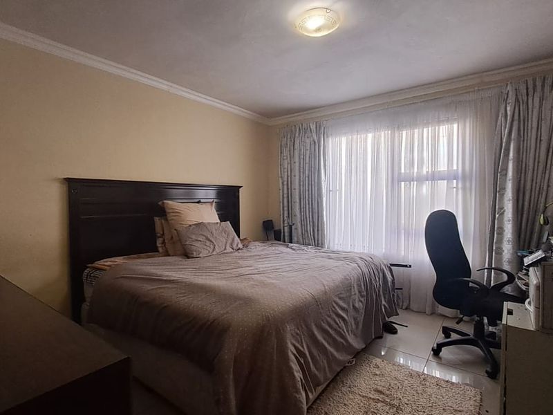 A standard bedroom featuring tiled flooring, crown molding, and large windows with curtain tracks, providing a functional living space.