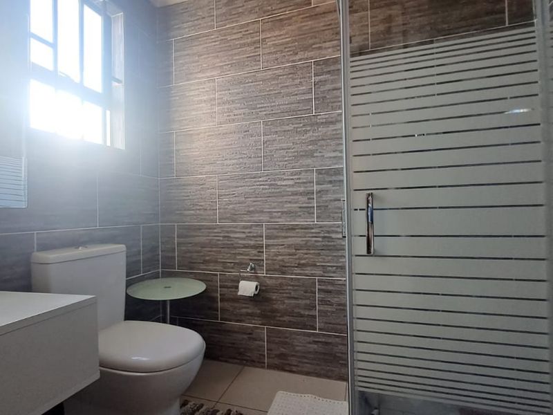 A modern bathroom featuring textured wall tiles, a glass-enclosed shower, a wall-mounted vanity with a vessel sink, and a dual-flush toilet.