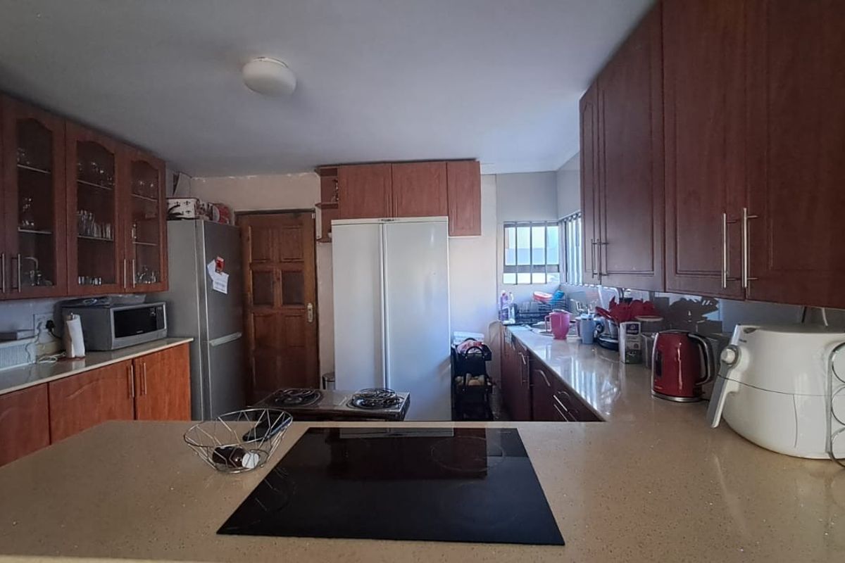 A functional kitchen featuring wooden cabinetry, stone-look countertops, and a built-in electric hob, offering ample storage and workspace for daily meal preparation.
