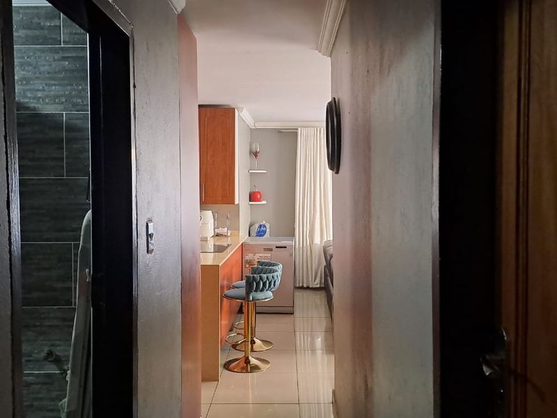 A view through a hallway looking into an open-plan kitchen and living area featuring tiled flooring and built-in cabinetry.