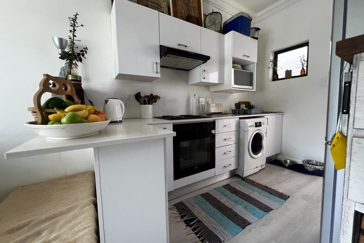 Compact kitchen featuring white cabinetry, integrated oven, extractor fan, and built-in laundry appliance space with light-toned flooring.