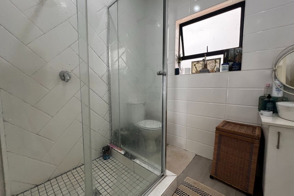 A functional bathroom featuring a glass-enclosed shower with herringbone wall tiling, a white vanity, and a top-hung window for natural ventilation.