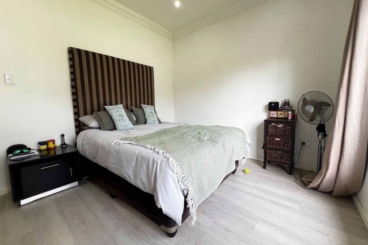 A well-maintained bedroom featuring light-toned laminate flooring, crown molding, and neutral wall finishes, providing a clean and comfortable living space.