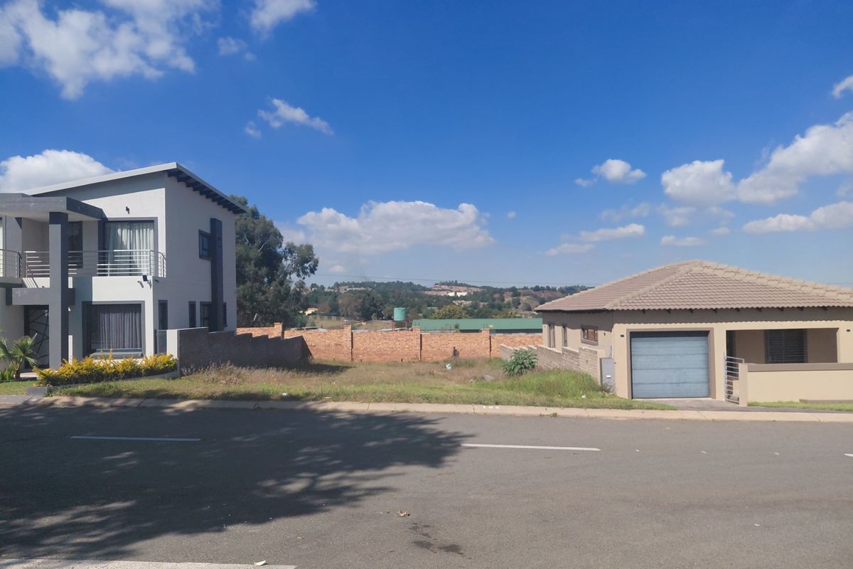 A vacant residential plot situated between two existing modern homes, featuring a brick boundary wall and street-level access in a developed neighborhood.