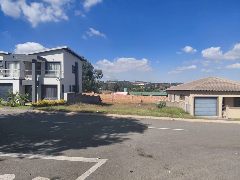 A vacant residential plot situated between two existing modern homes, featuring established boundary walls and street access in a developed neighborhood.