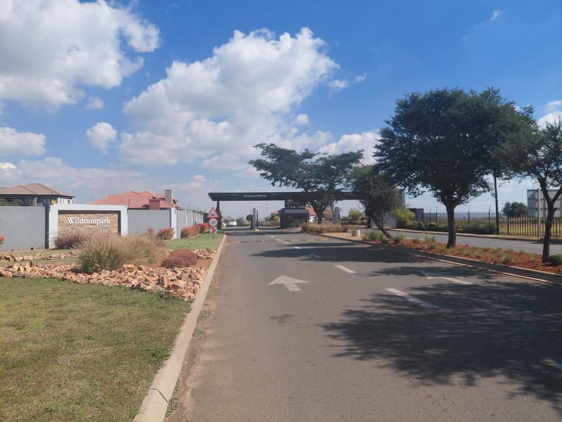 Entrance view of Wildtuinpark Estate featuring a paved access road, security gatehouse, and landscaped perimeter walling.