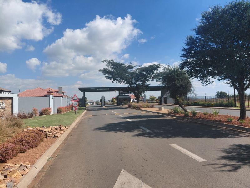 A view of the secure gated entrance and access road leading into the residential estate, featuring paved roads and landscaped verges.