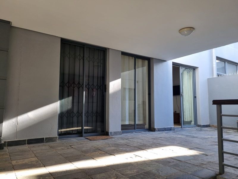 A covered patio area featuring stone tile flooring and multiple sliding glass doors providing access to the interior living spaces.