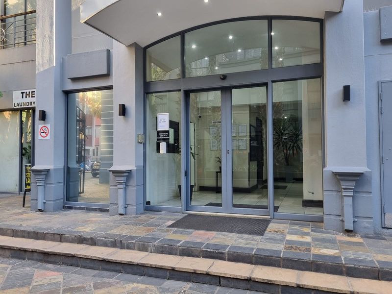 The main entrance of the apartment building features a modern glass door system, stone-tiled steps, and exterior wall-mounted lighting.