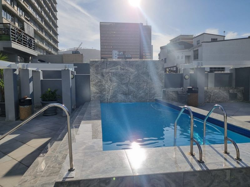 A well-maintained rooftop swimming pool area featuring tiled surrounds, a decorative stone-cladded water feature, and stainless steel access ladders.
