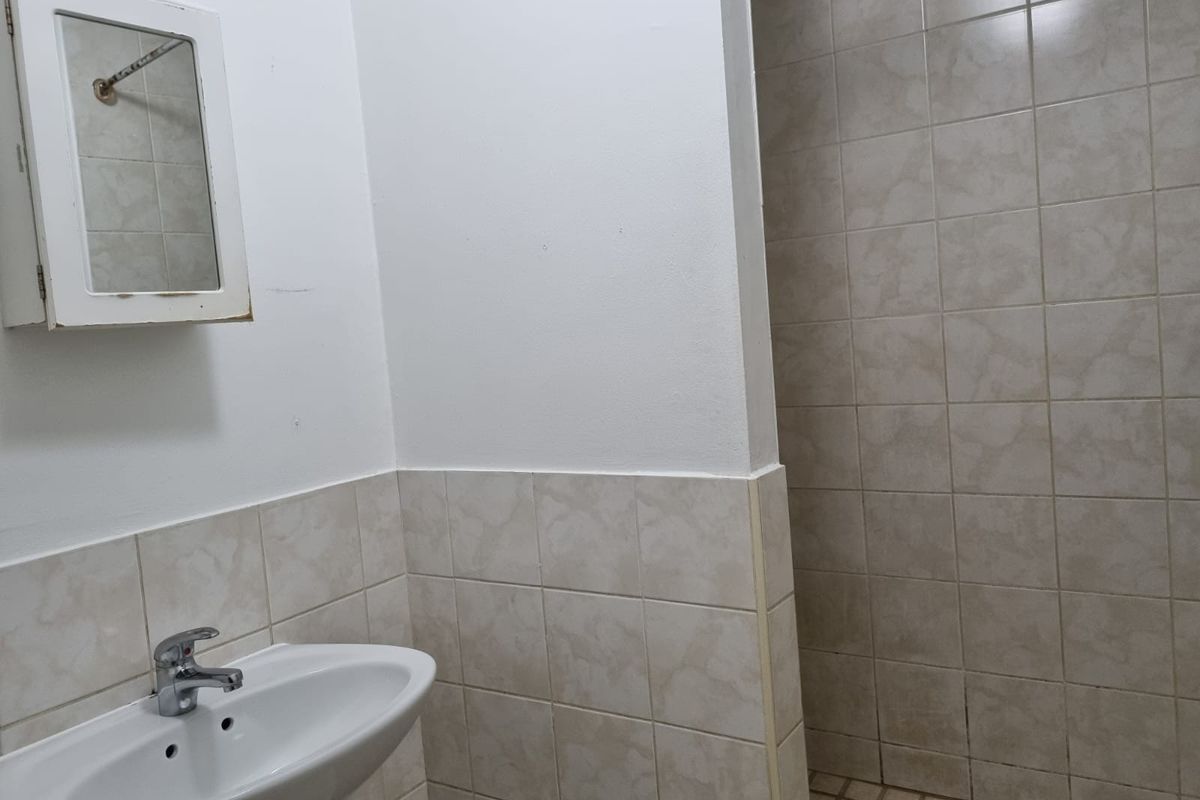 A functional bathroom featuring a pedestal basin, wall-mounted medicine cabinet, and a tiled shower enclosure.