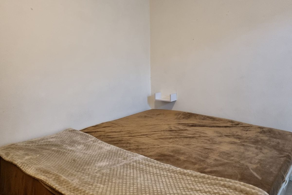 A simple bedroom featuring a wall-mounted floating shelf and neutral wall finishes.