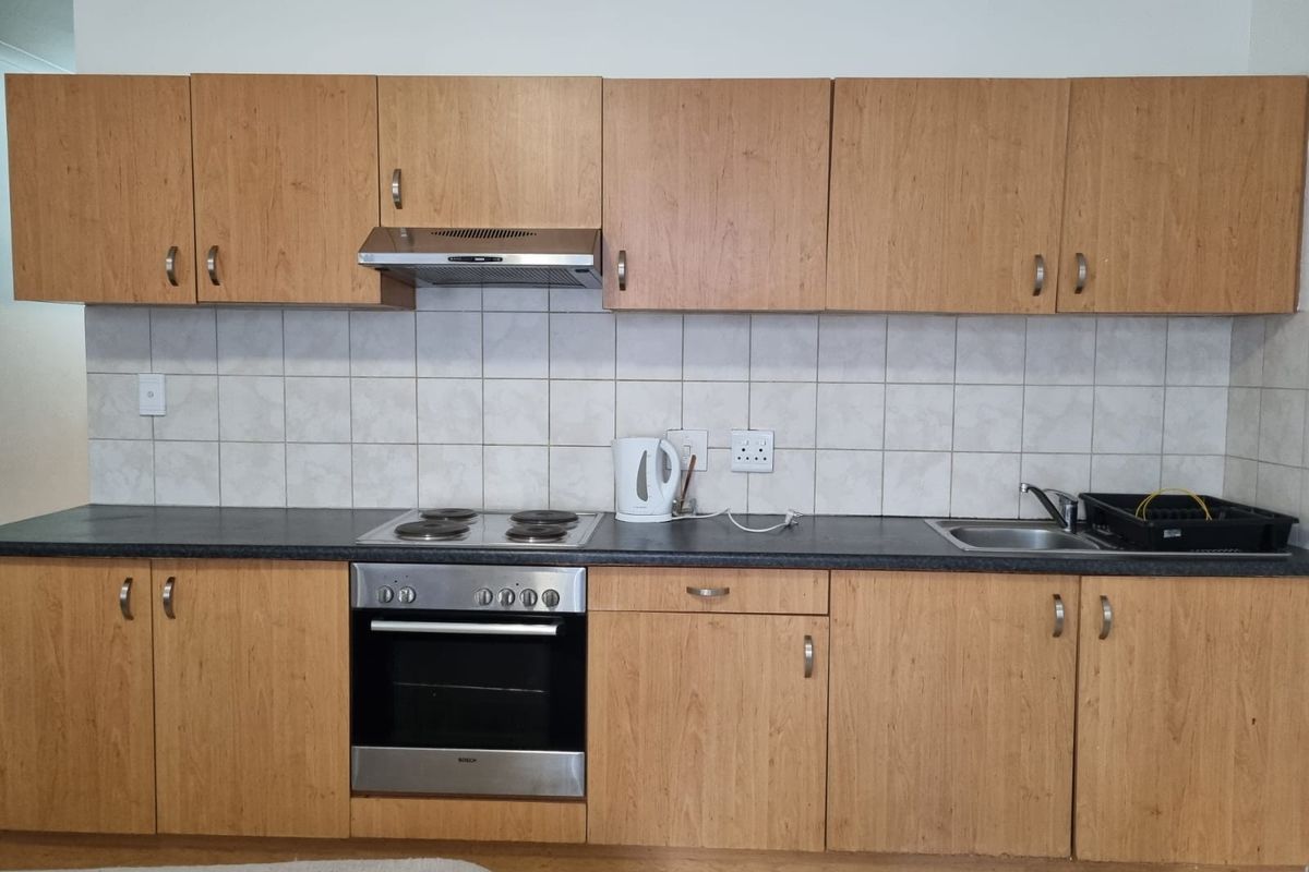 A functional kitchen featuring light wood cabinetry, a built-in oven, electric hob, extractor fan, and a stainless steel sink with tiled backsplash.