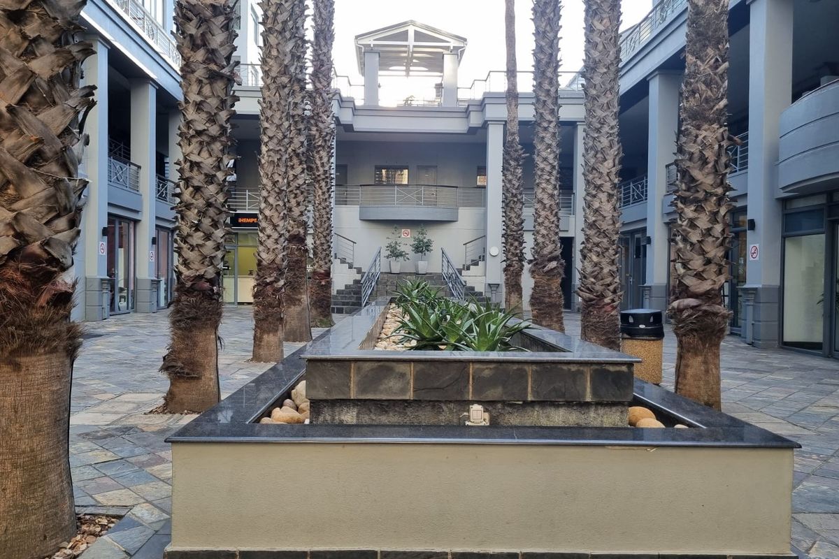 A well-maintained central courtyard featuring stone paving, mature palm trees, and a central stone-clad water feature within an apartment complex.