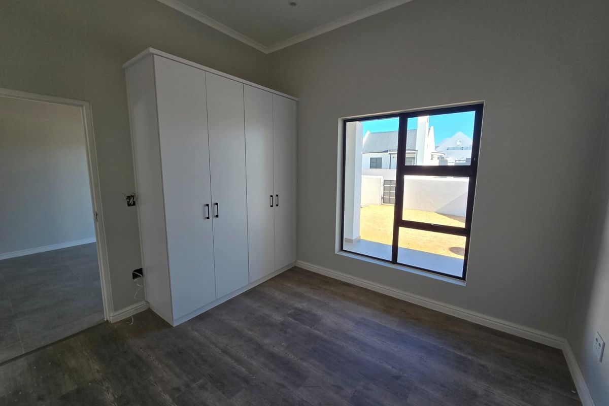 A bright, modern bedroom featuring neutral walls, durable laminate flooring, and sleek built-in cupboards, offering a clean and versatile living space.