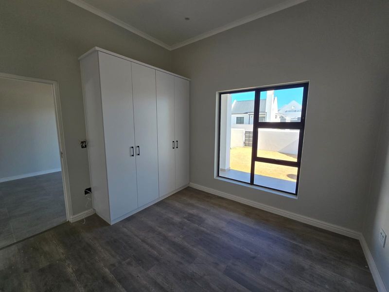 A bright, modern bedroom featuring neutral walls, durable laminate flooring, and sleek built-in cupboards, offering a clean and versatile living space.