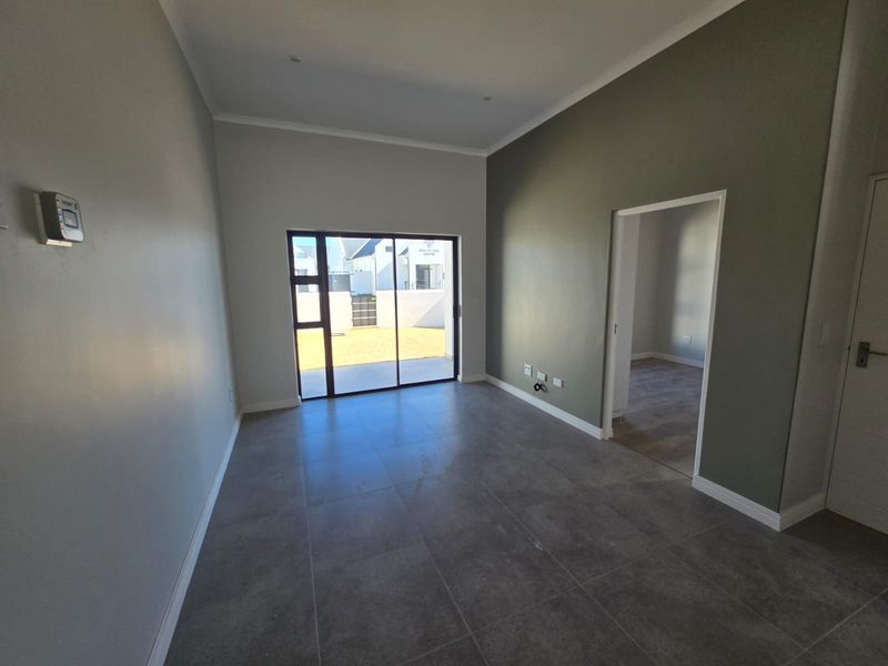 A bright, empty living room featuring large format floor tiles, neutral walls, and a sliding glass door providing access to the rear exterior.