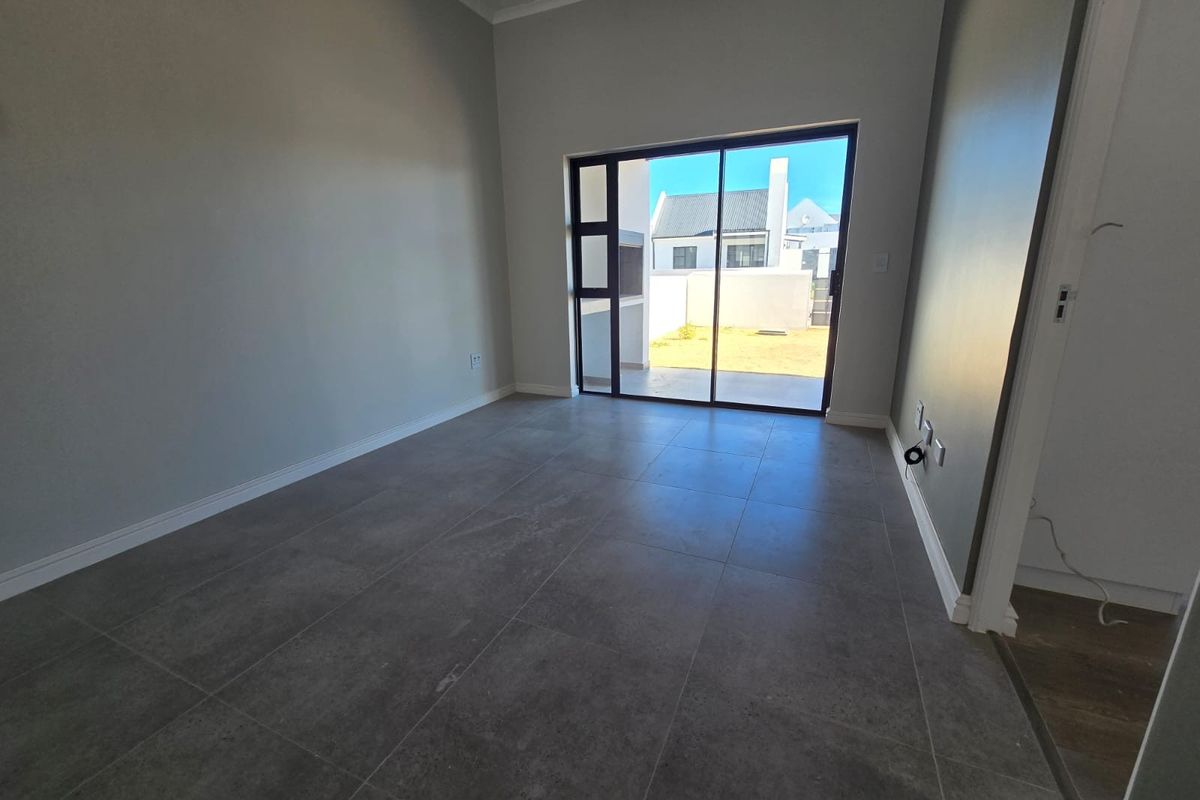 An empty living room featuring modern grey floor tiles, neutral walls, and a large sliding glass door providing access to the rear patio.