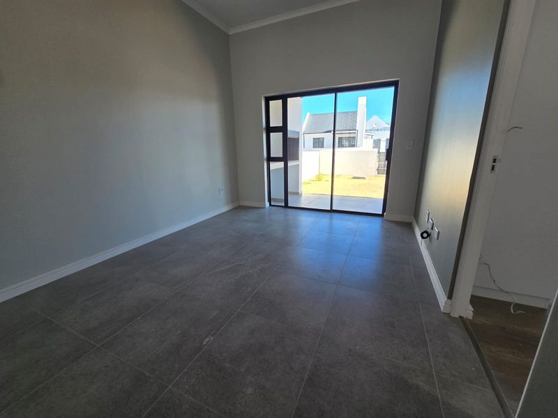 An empty living room featuring modern grey floor tiles, neutral walls, and a large sliding glass door providing access to the rear patio.
