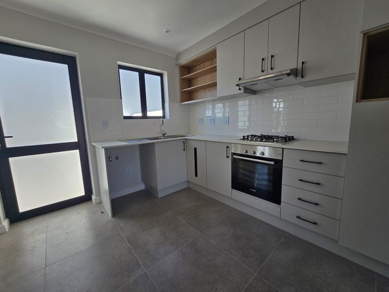 Modern kitchen featuring light grey cabinetry, stone countertops, subway tile backsplash, and integrated stainless steel appliances including a gas hob and oven.