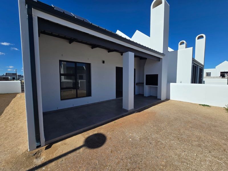 A modern covered patio featuring a built-in braai, tiled flooring, and a clean white exterior finish, perfect for outdoor entertaining.