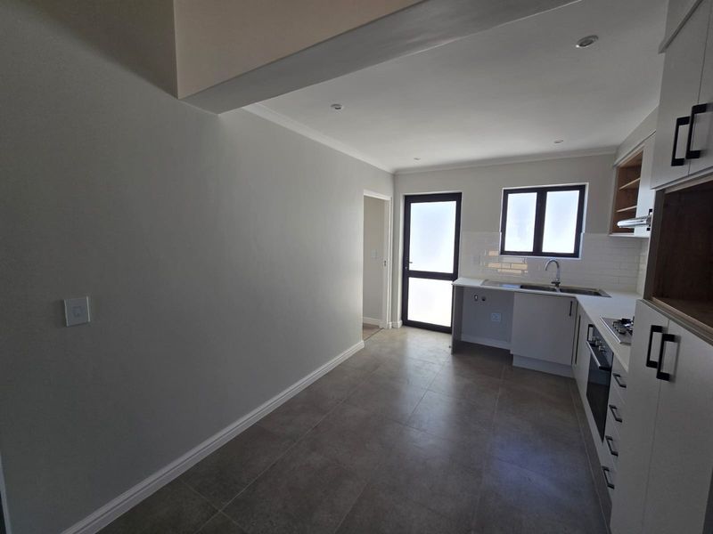 Modern kitchen featuring neutral cabinetry, tiled splashback, built-in oven and hob, and tiled flooring, offering a clean and functional workspace.