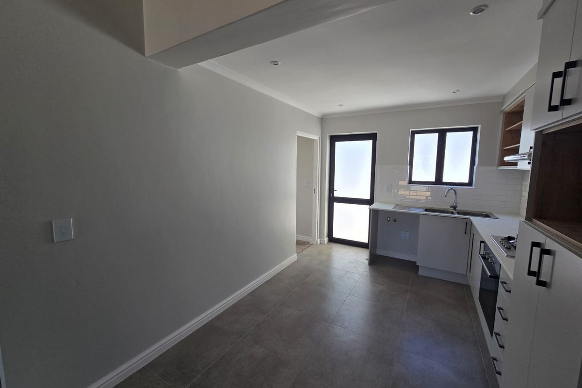 Modern kitchen featuring neutral cabinetry, tiled splashback, built-in oven and hob, and tiled flooring, offering a clean and functional workspace.