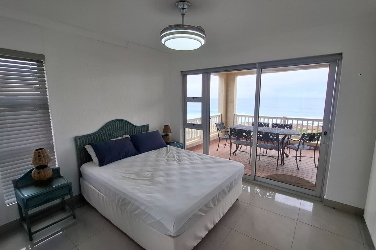 A bedroom featuring tiled flooring, built-in cupboards, and sliding glass doors that open onto a balcony with ocean views.
