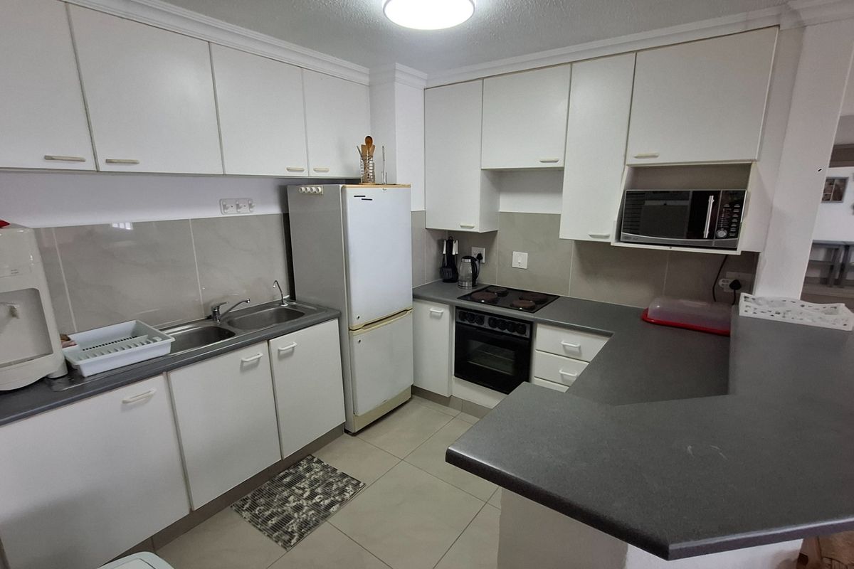 A functional kitchen featuring white cabinetry, dark laminate countertops, a built-in oven, and a ceramic hob with an integrated breakfast bar.