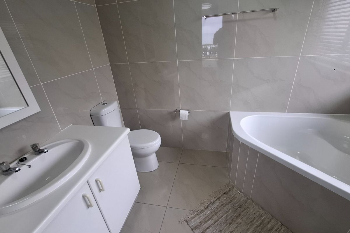 A modern bathroom featuring neutral wall tiles, a corner bathtub, a vanity with an integrated basin, and a toilet.