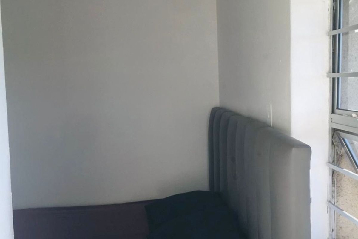 A compact bedroom featuring a window with security bars and neutral wall finishes.