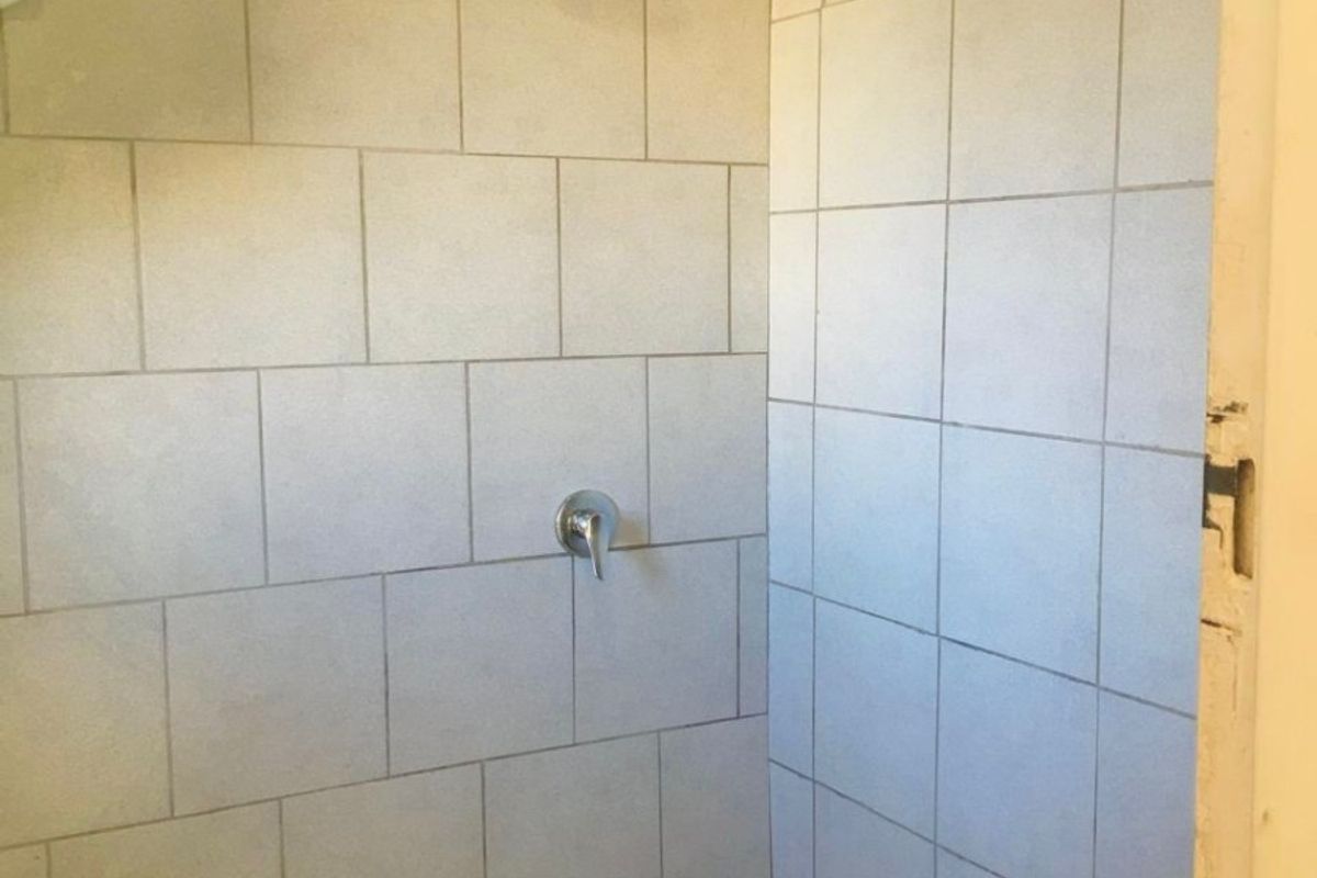 A basic shower enclosure featuring tiled walls and floor, currently requiring maintenance and the installation of a shower screen or door.