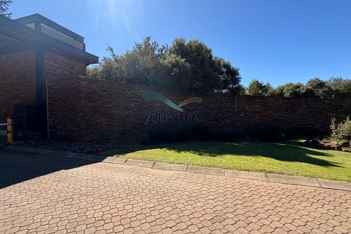 Entrance view of the Vulintaba Country Estate featuring a stone boundary wall, paved driveway, and manicured landscaping at the security access point.