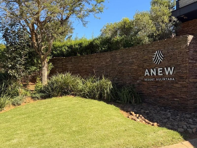 A well-maintained stone feature wall with resort signage, surrounded by landscaped garden beds and manicured lawn at the property entrance.