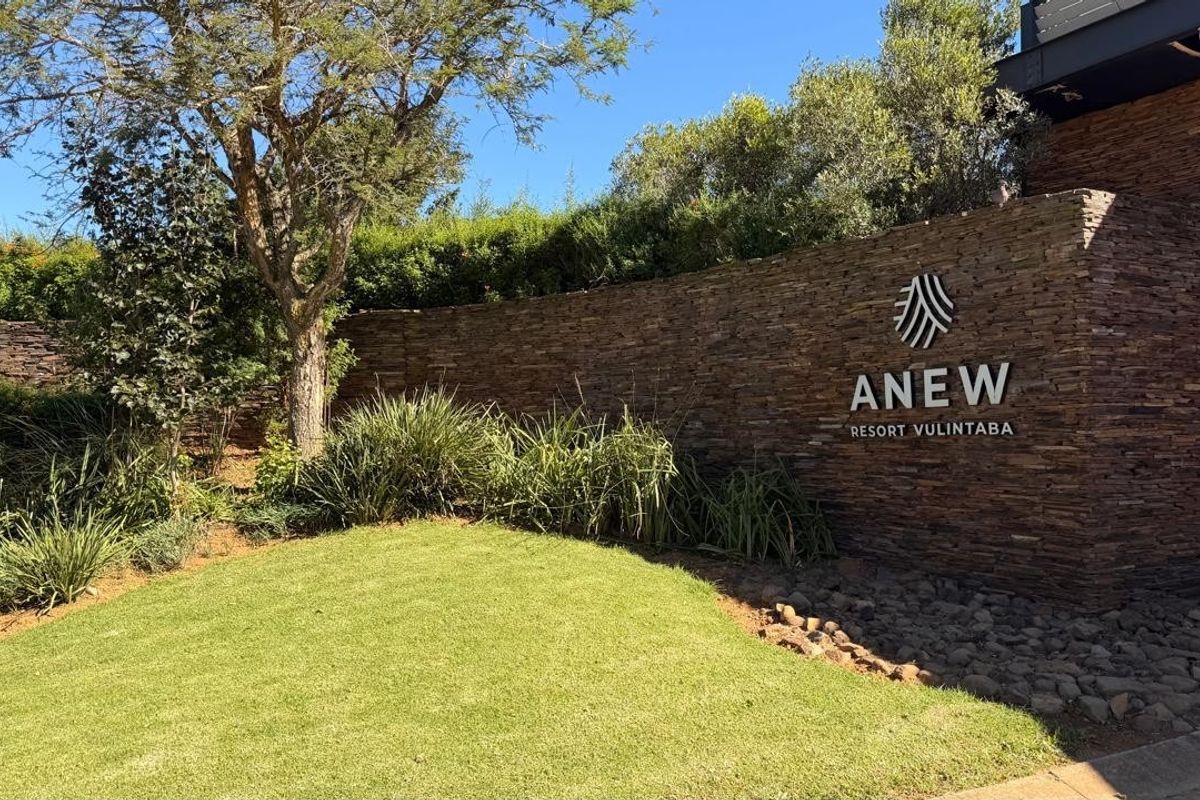 A well-maintained stone feature wall with resort signage, surrounded by landscaped garden beds and manicured lawn at the property entrance.