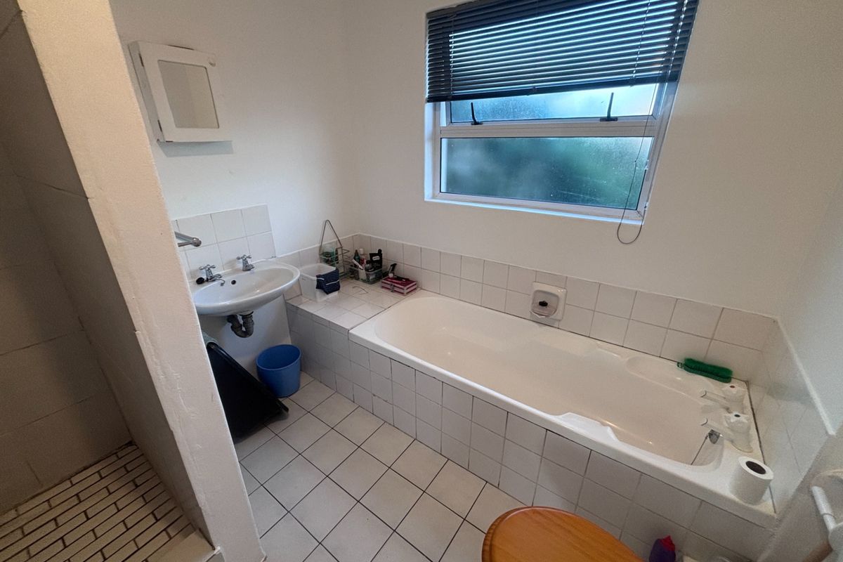 A functional bathroom featuring a built-in bathtub, pedestal sink, and separate shower area with tiled finishes and a window for natural light.