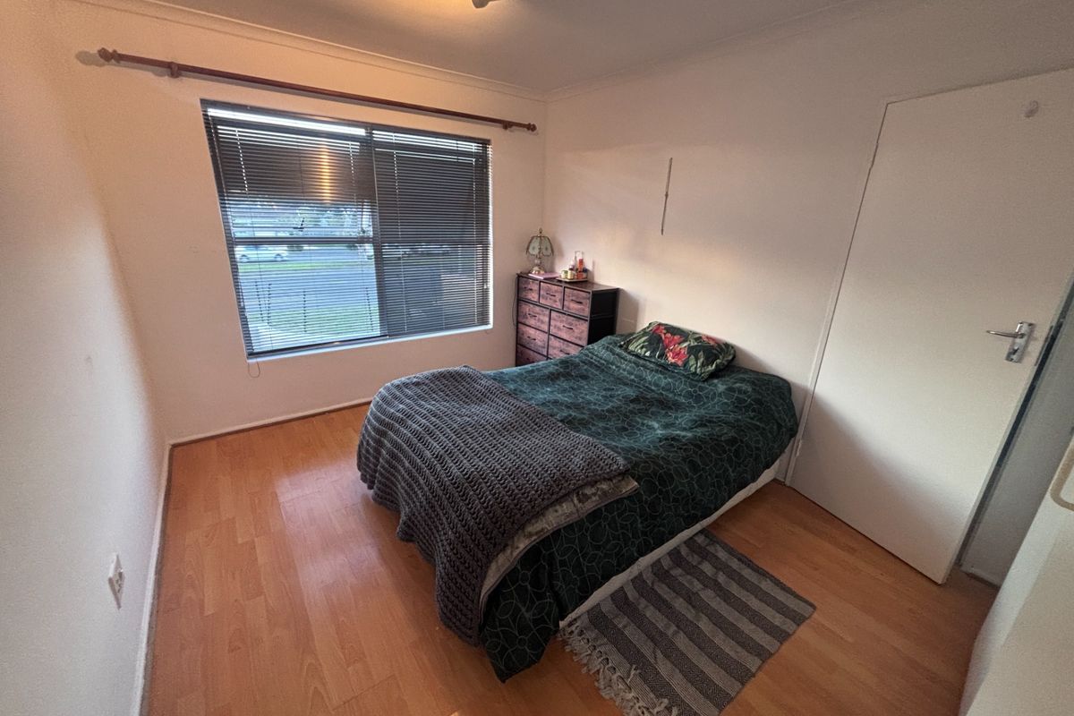 A standard bedroom featuring laminate wood flooring, a large window with blinds, and a built-in door.