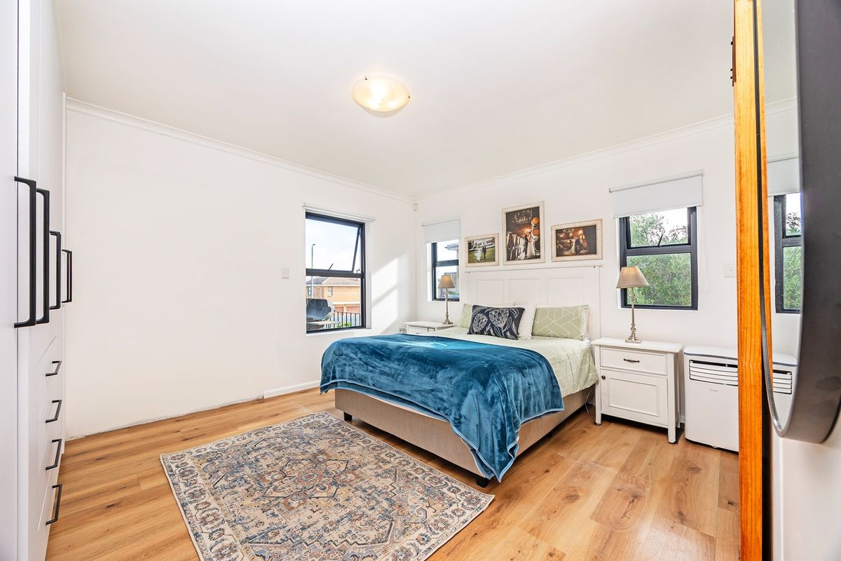 A bright and well-maintained bedroom featuring timber flooring, built-in cabinetry, and large windows that provide ample natural light.