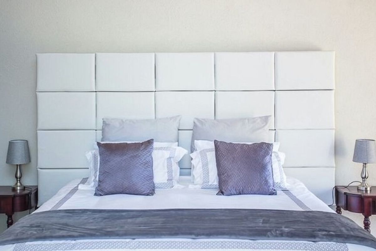 A well-maintained bedroom featuring a large, modern white upholstered headboard as a central design element.