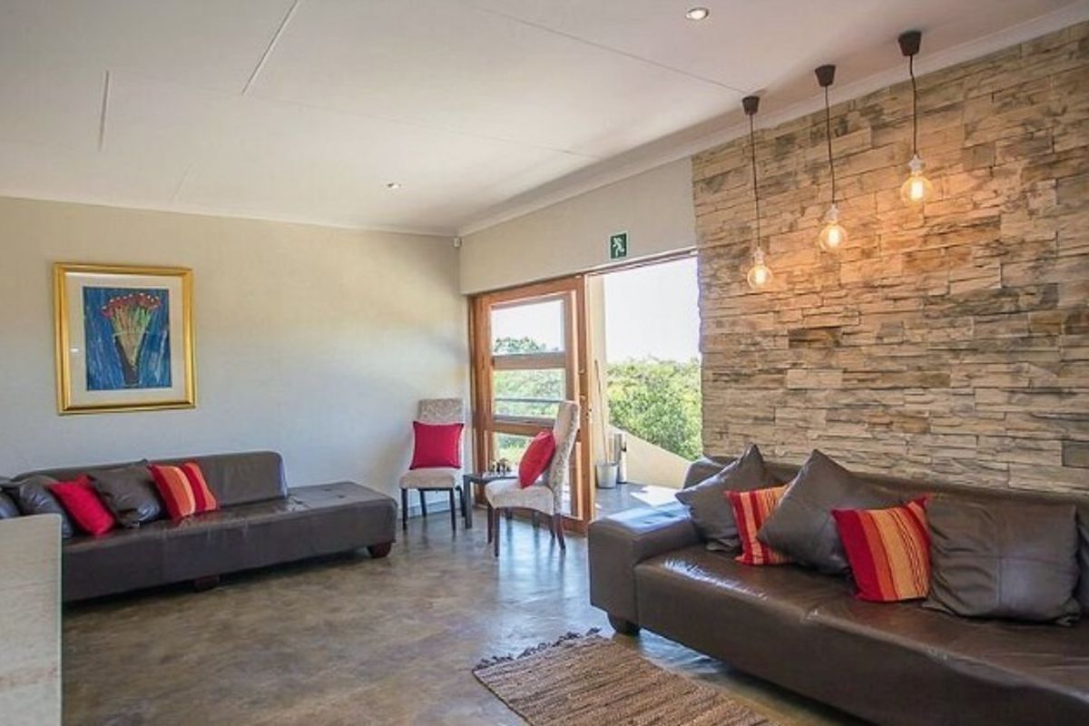 Spacious living area featuring a prominent natural stone feature wall, polished concrete flooring, and large glass doors leading to an outdoor space.