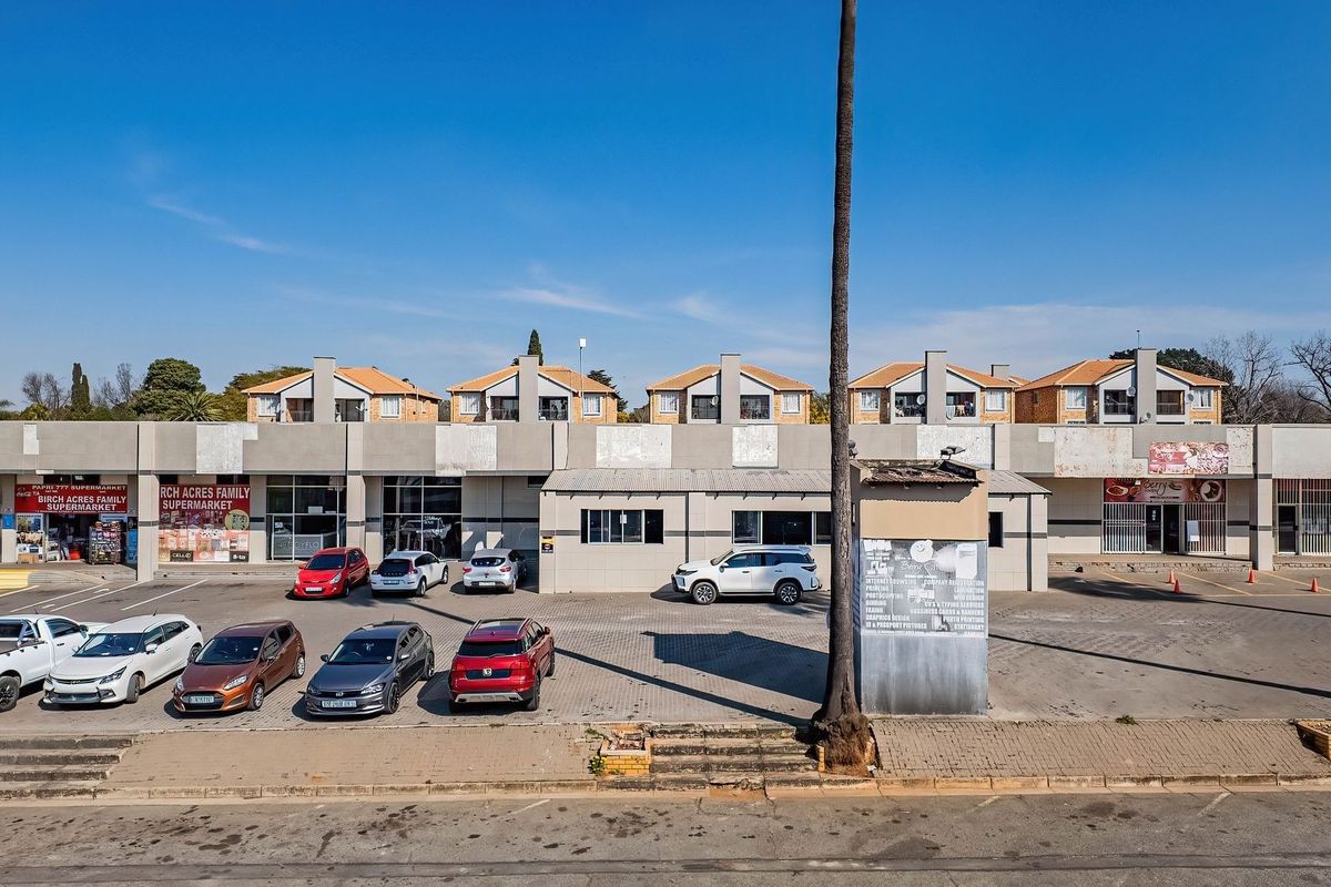 Aerial view of a commercial strip mall featuring multiple storefronts, a paved parking lot, and concrete facade elements.