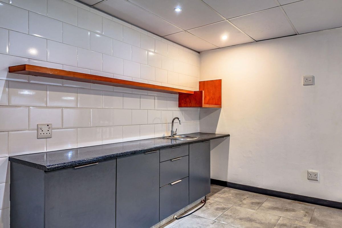 A functional kitchenette featuring dark grey cabinetry, a granite countertop, stainless steel sink, and white subway tile backsplash with integrated wooden shelving.