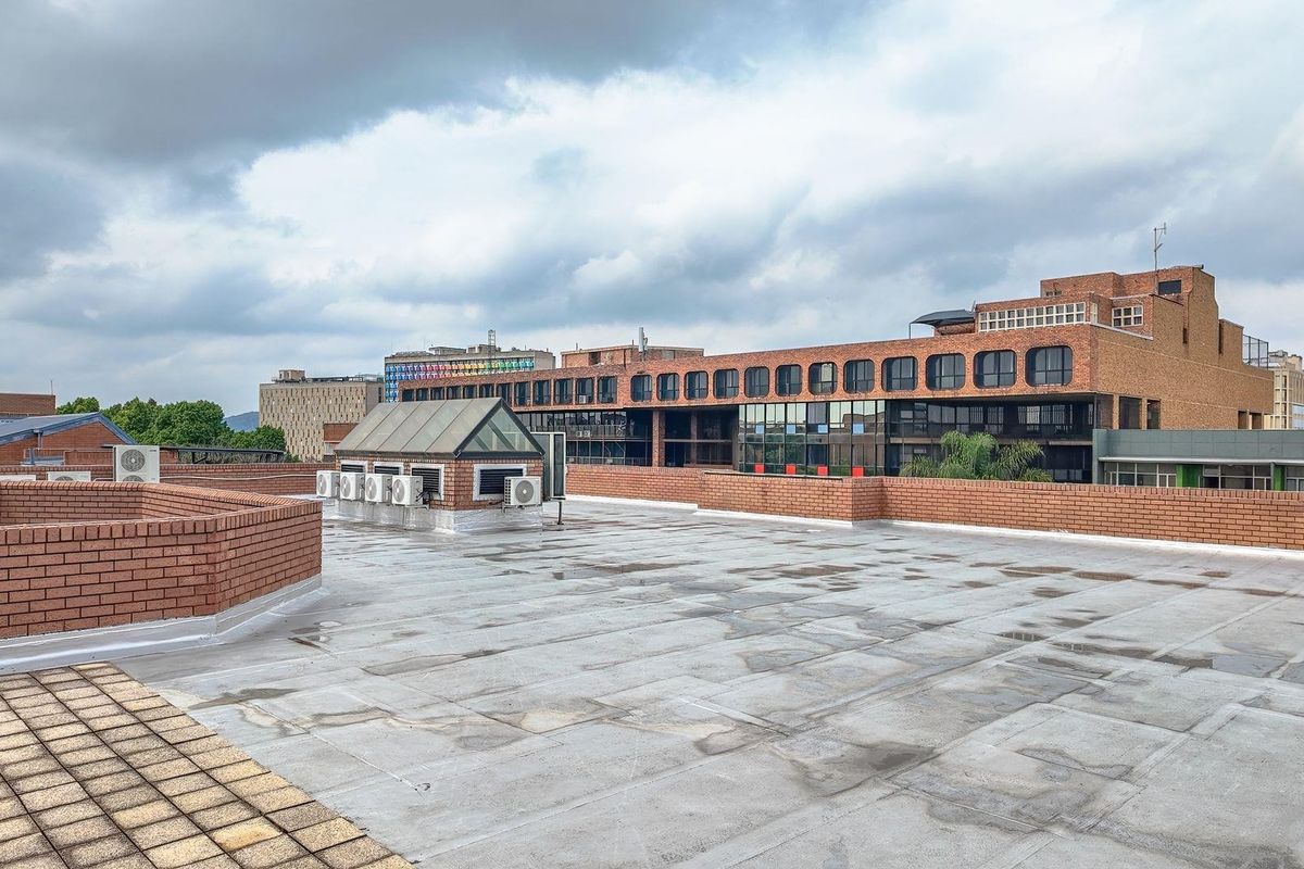 A spacious rooftop terrace featuring brick parapet walls, a skylight structure, and multiple external air conditioning units, offering an expansive view of the surrounding urban area.