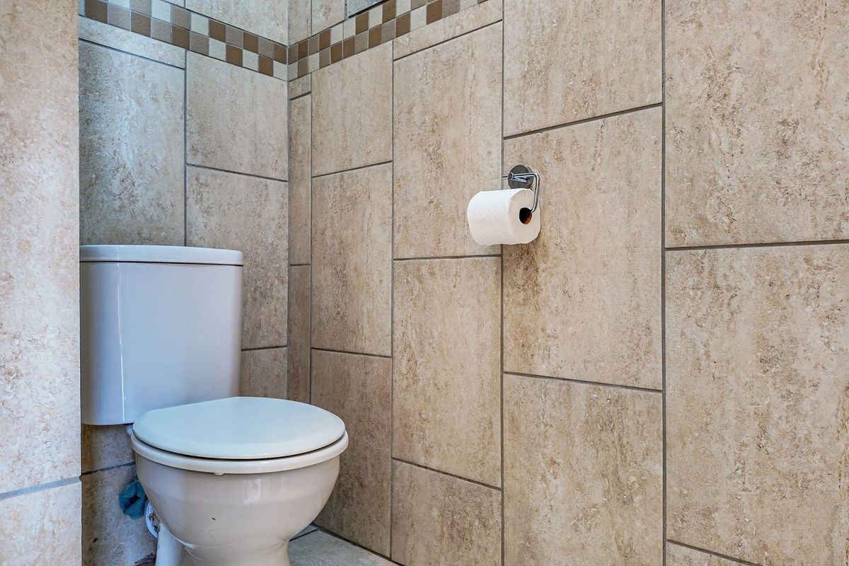 A compact bathroom featuring floor-to-ceiling neutral stone-look wall tiles and a standard white ceramic toilet suite.