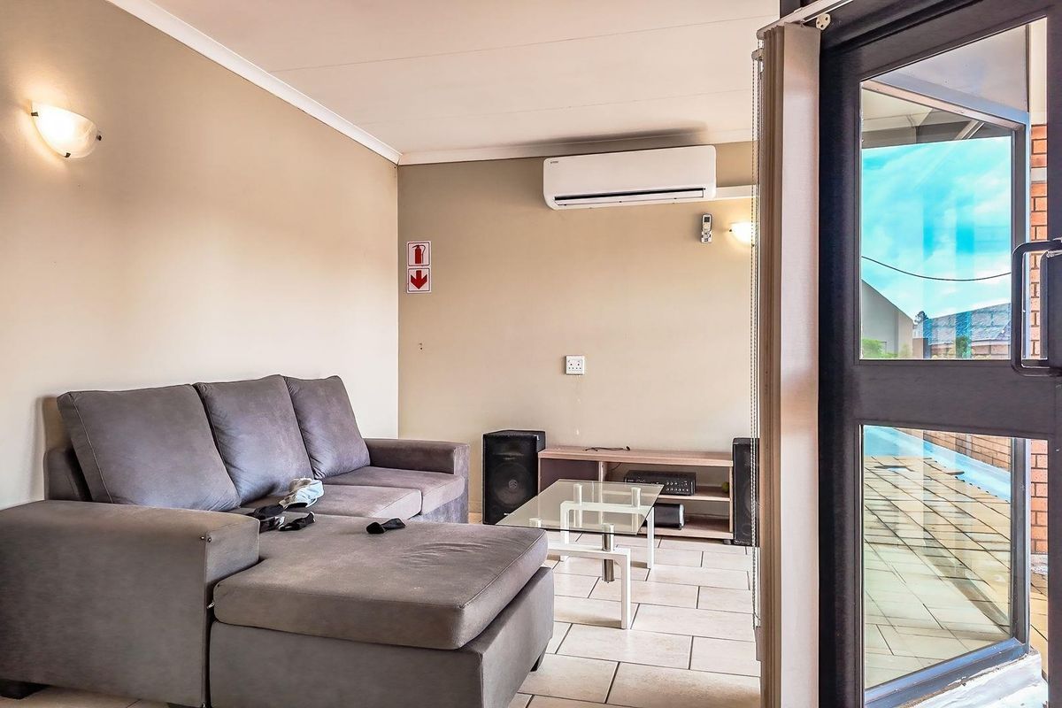 A functional living area featuring tiled flooring, a wall-mounted air conditioning unit, and direct access to an outdoor patio through a glass door.