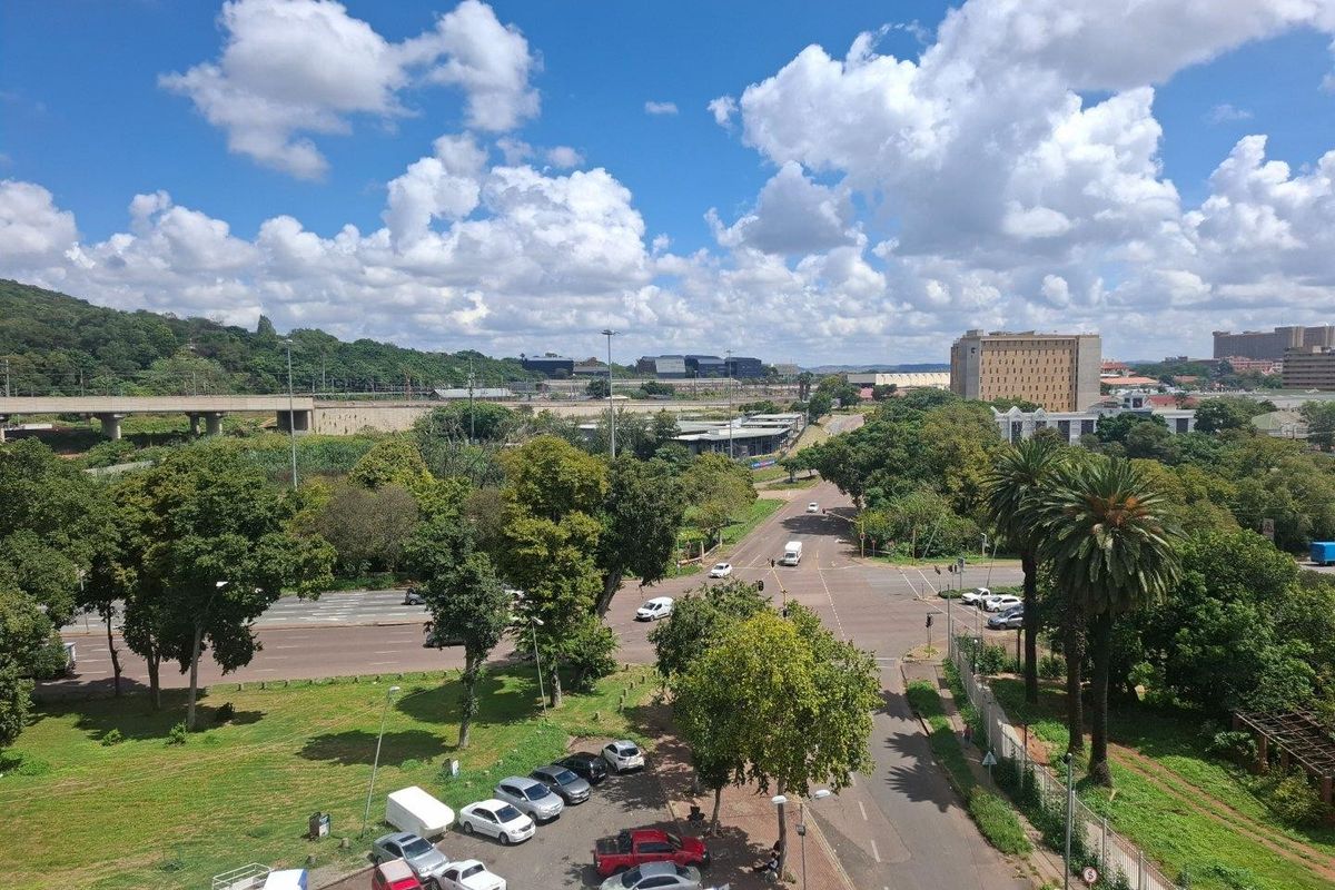 Elevated aerial view overlooking a commercial intersection, surrounding greenery, and urban infrastructure with clear sky conditions.