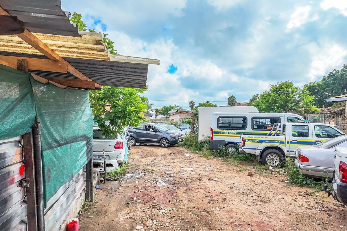 An exterior view of a commercial property featuring an unpaved yard area with makeshift structures and parking space.